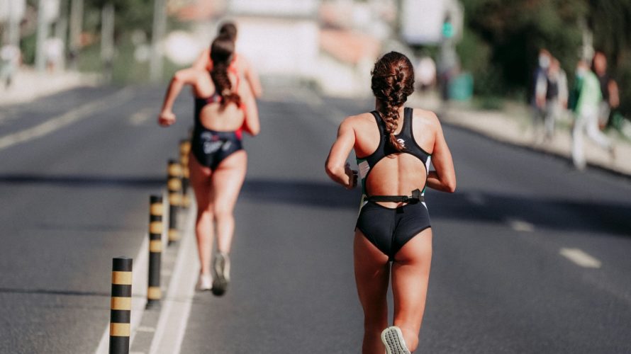 faceless sportswomen running on asphalt road in daytime